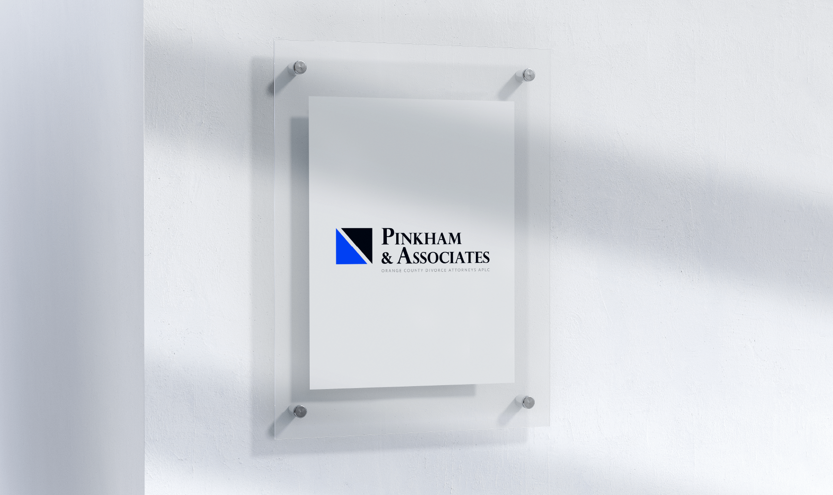 A frosted glass wall sign displays the logo for Pinkham & Associates with a black and blue geometric design, mounted with four metal standoffs on a white wall.