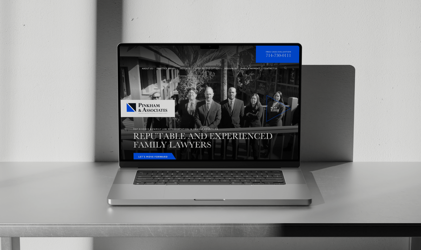 A laptop on a gray desk displays the Pinkham & Associates All website, featuring a black-and-white photo of four people and text reading Reputable and Experienced Family Lawyers.